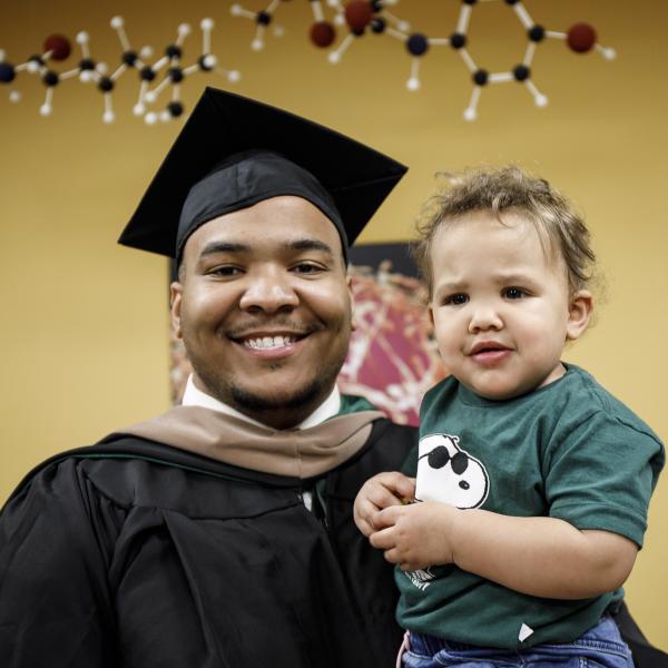 Smiling graduate in cap and gown holding a child