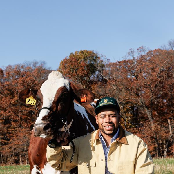 Darian Poles, a previous student is in the fields with a cow beside him. 