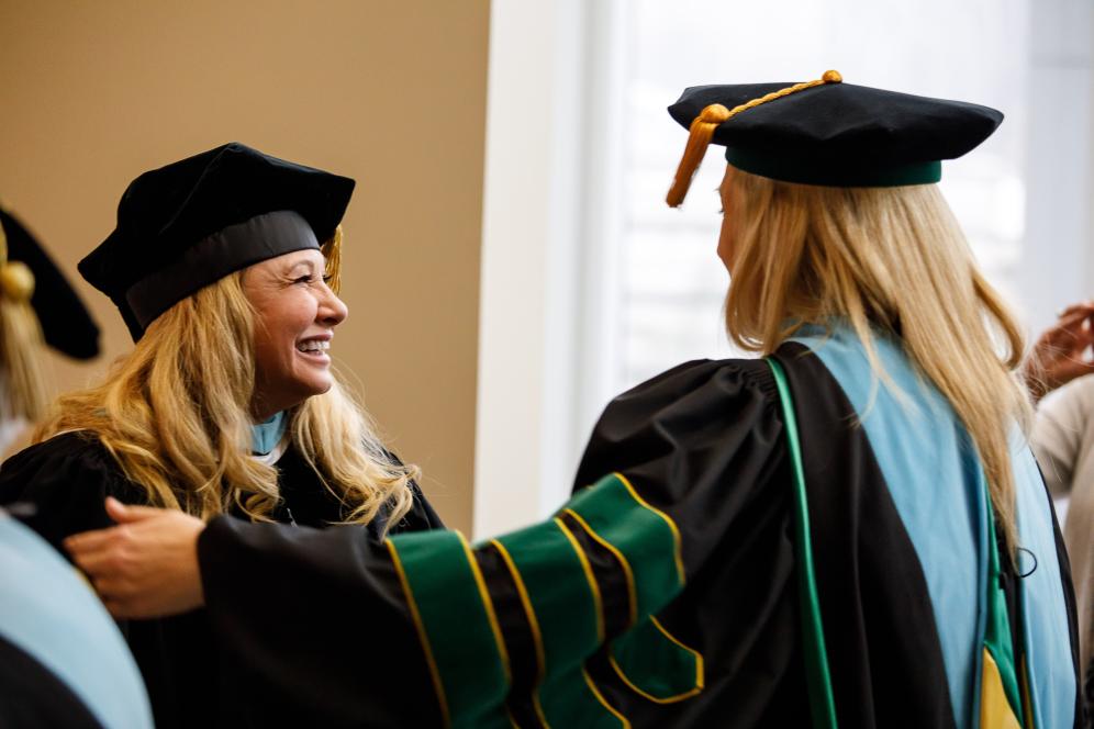 Graduate students dressed in cap and gown greet each other. 