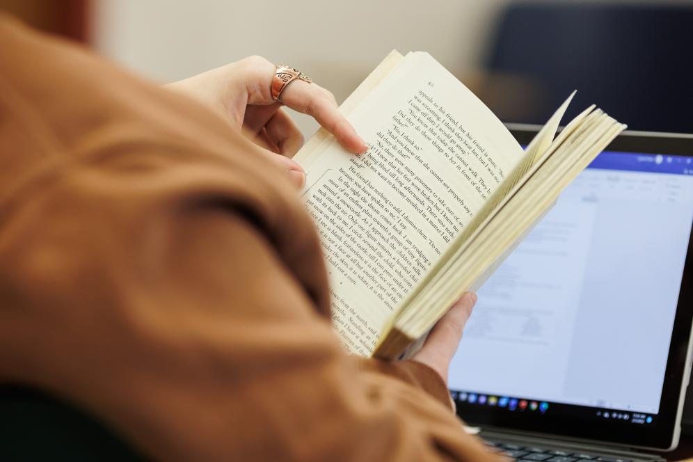 An image from over a students shoulder of an open book and laptop