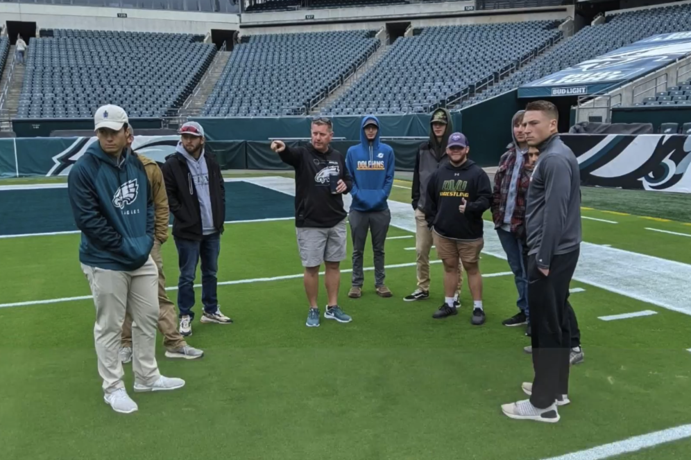 Students are on a professional football field learning from a groundskeeper.