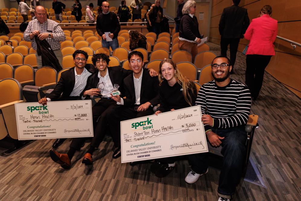 three representatives from Horus Health, Katia Holmes '27, and Cory Korkins '25 are seated for a photo with a giant check