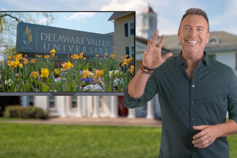 Alex Boylan is seen waving at the camera standing on the campus quad.